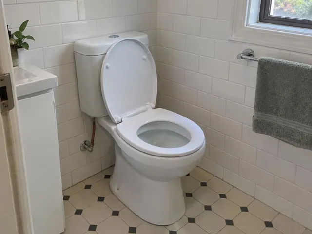 Clean white toilet in a tiled bathroom with towel rail and window in Coogee