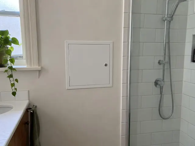 Bathroom wall with a small access panel beside a tiled shower and window in Kensington